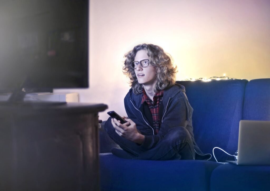 pexels-photo-3811814 Concentrated male with long hair sitting on comfortable sofa at home and messaging on social media via cellphone while watching movie on TV with opened mouth
